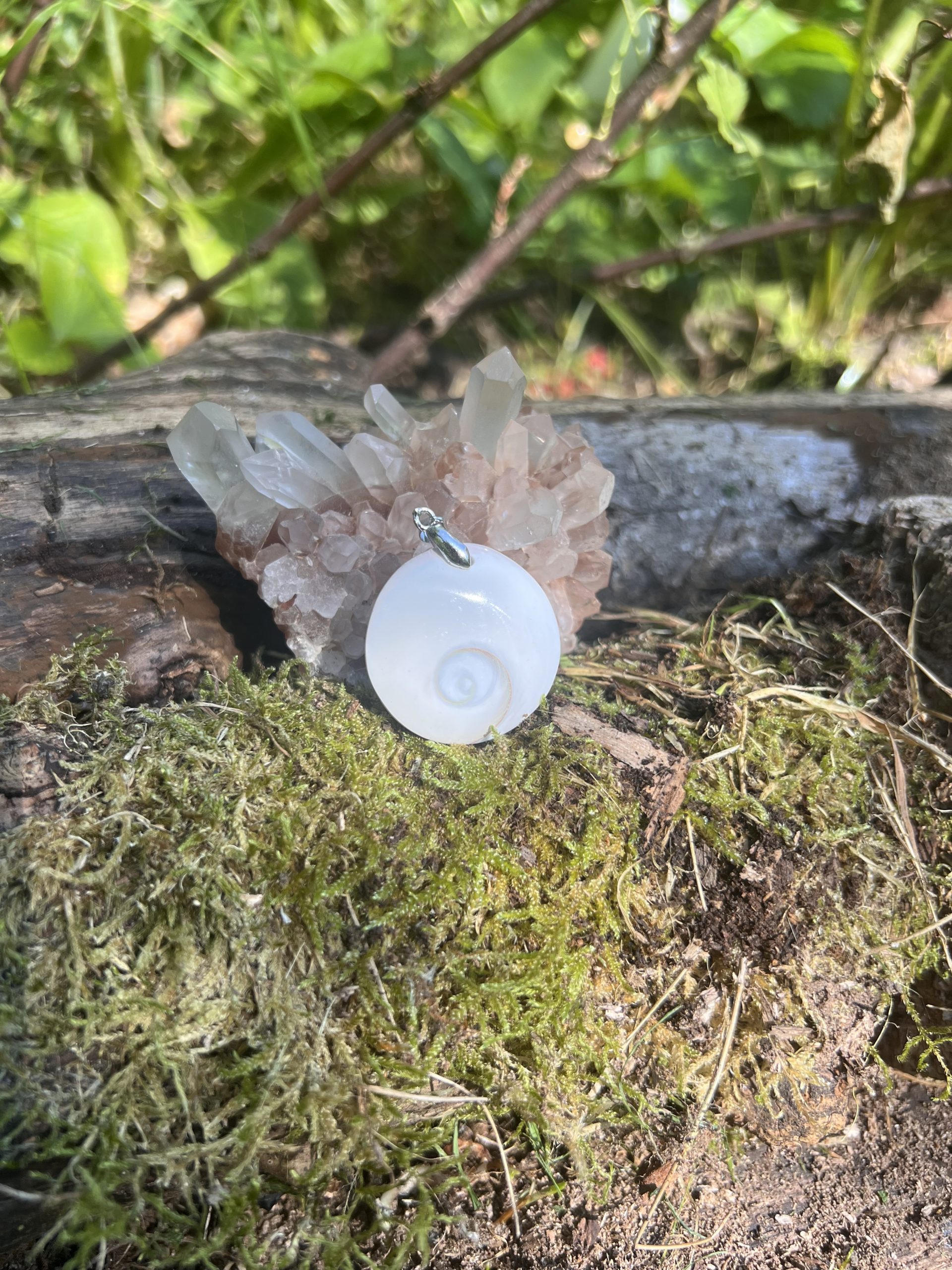 Pendentif naturel en Œil de Shiva posé sur un lit de mousse avec un amas de quartz en fond – photo prise en extérieur